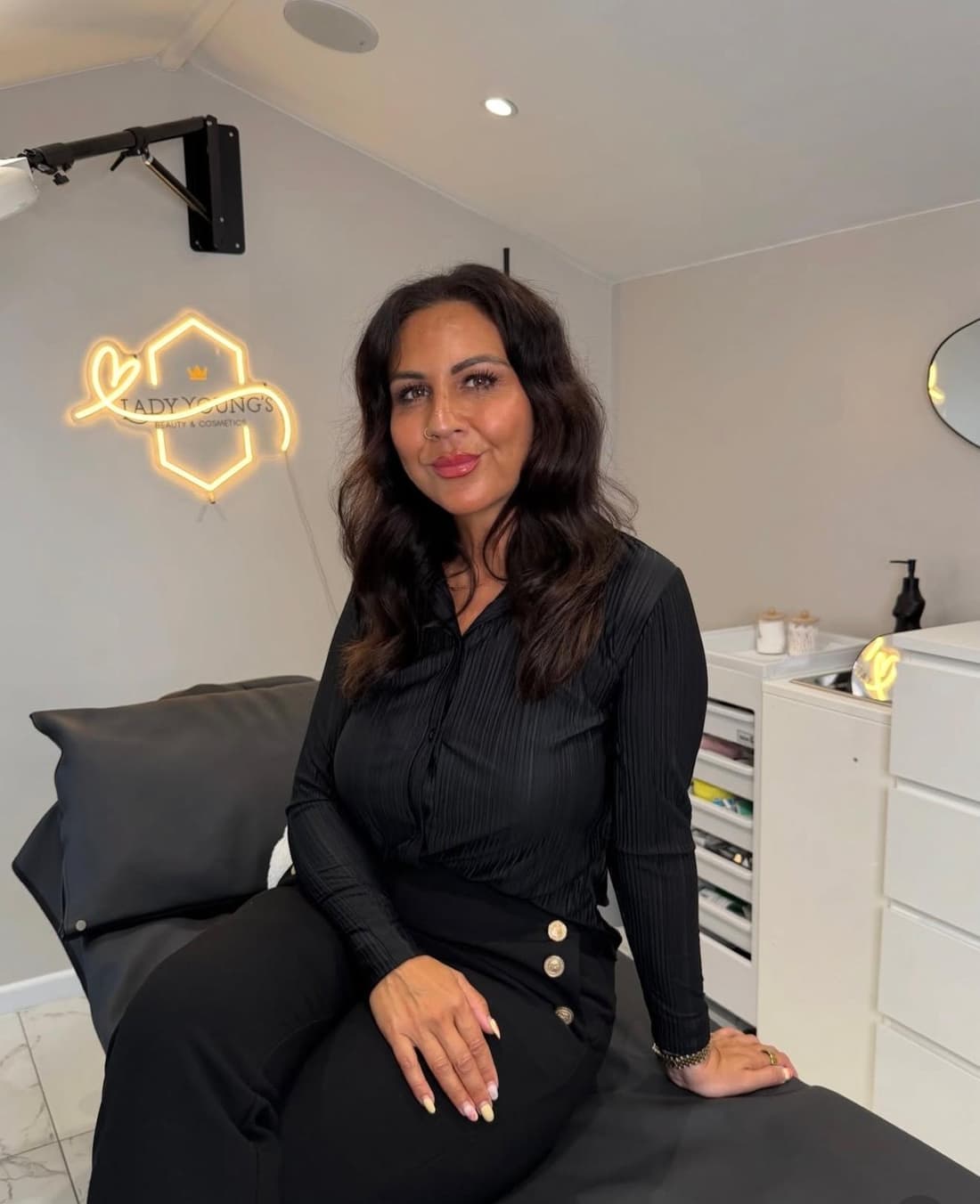 Safina Young in her Lady Young's Beauty & Cosmetics studio in Bracknell, beside the gold neon clinic sign